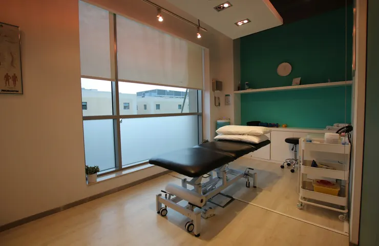 Una sala de fisioterapia luminosa con una camilla y una ventana grande