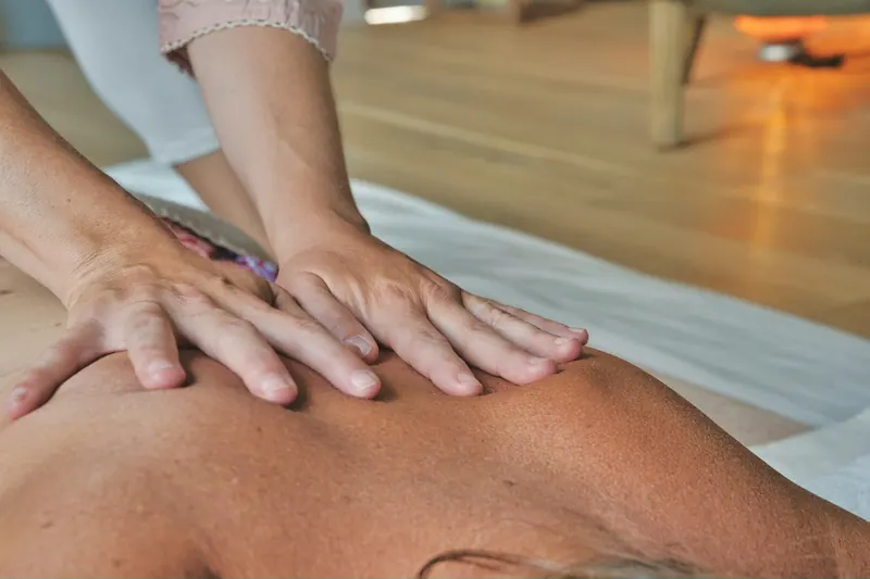 Dos manos dan un masaje en la espalda de una persona tumbada